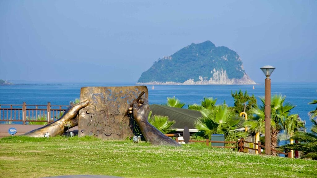 Bronze hands sculpture in Jaguri Park stands before Seopseom Island and the blue sea.