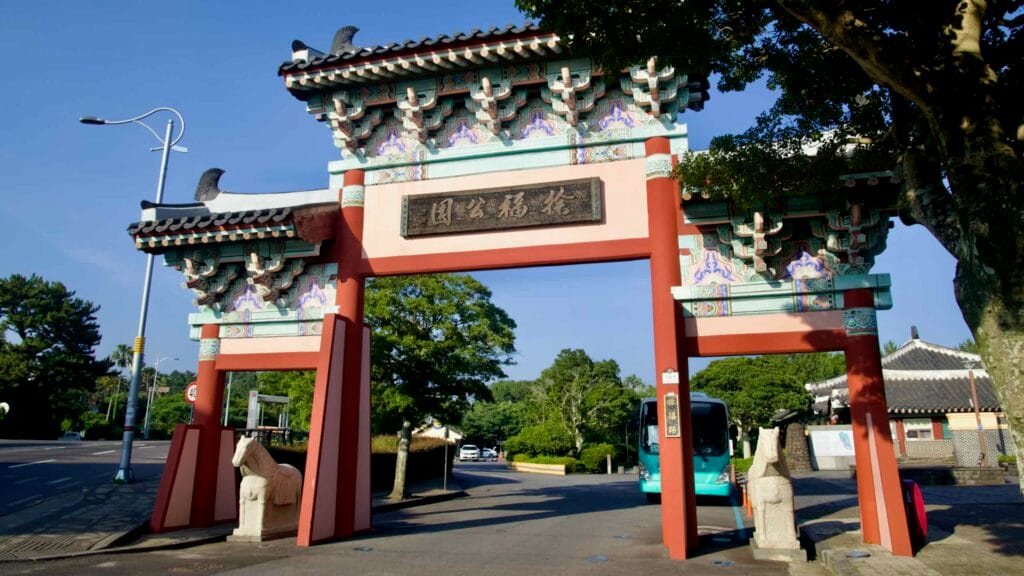An ornate traditional gateway with stone horse statues marks the Jeongbang Falls area entrance.