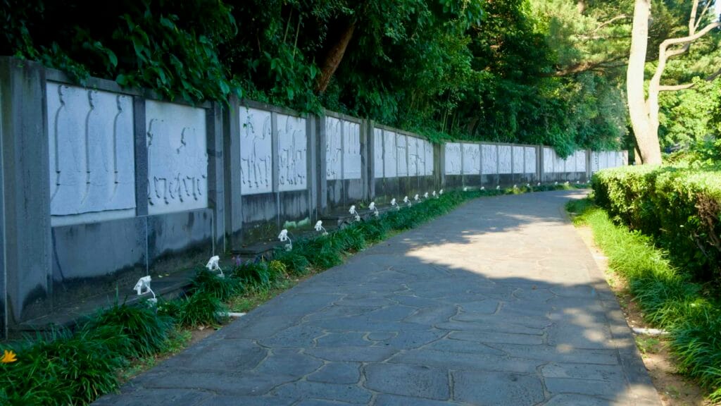 Carved stone relief panels line a shaded garden wall near Jeongbang Falls.