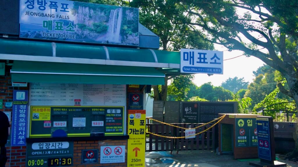 The Jeongbang Falls ticket office shows admission information and rules at the park entrance in Seogwipo.