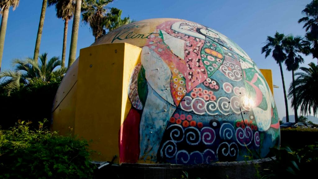 A painted dome signed “Klimt” stands among coastal palms.
