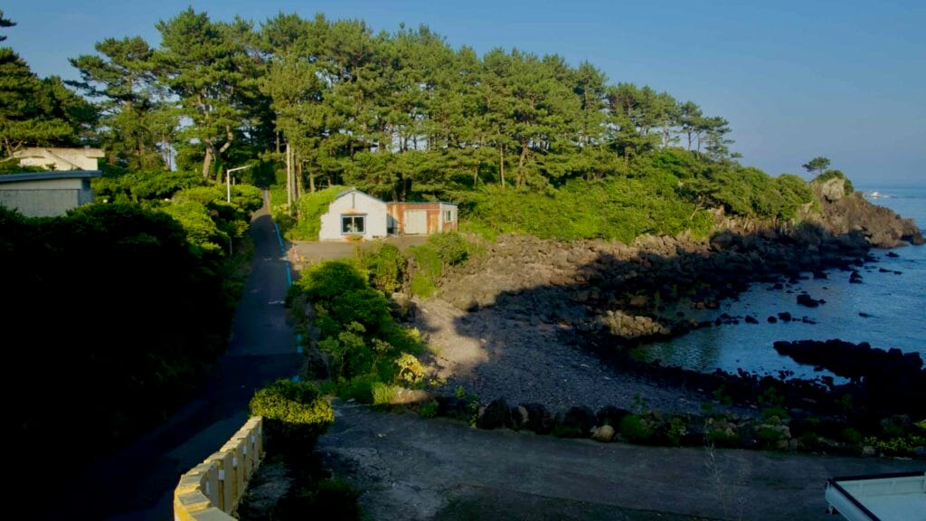 A pine‑shaded cove and pebble beach sit below cottages.
