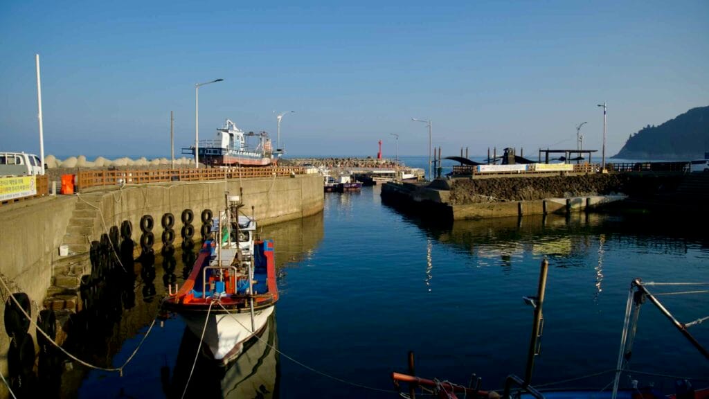 Boats moor inside a harbor channel with a red lighthouse.