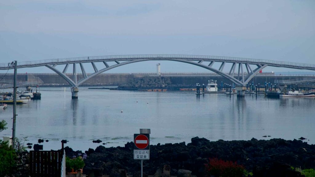 Saeyeongyo Bridge links Seogwipo Port to Saeseom above calm harbor water.