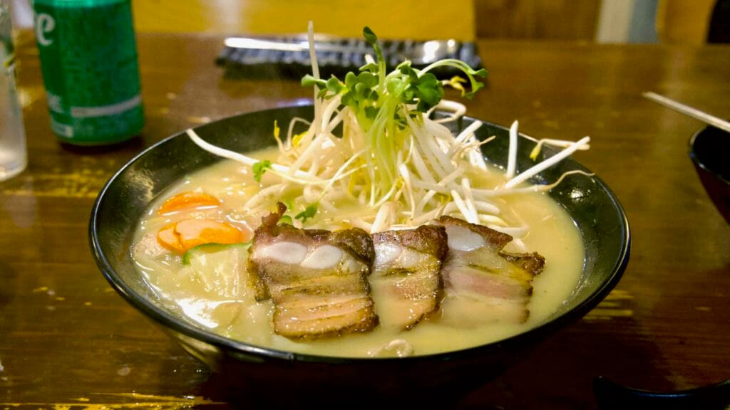 A steaming ramen bowl with pork belly and sprouts at a Seogwipo eatery.