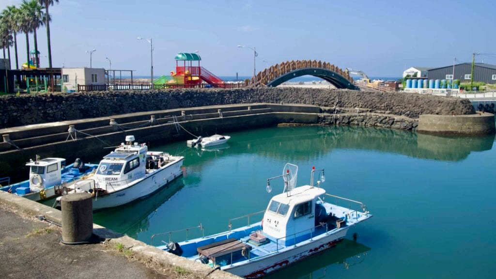 Fishing boats rest below an arched bridge and playground in Namwon Port.