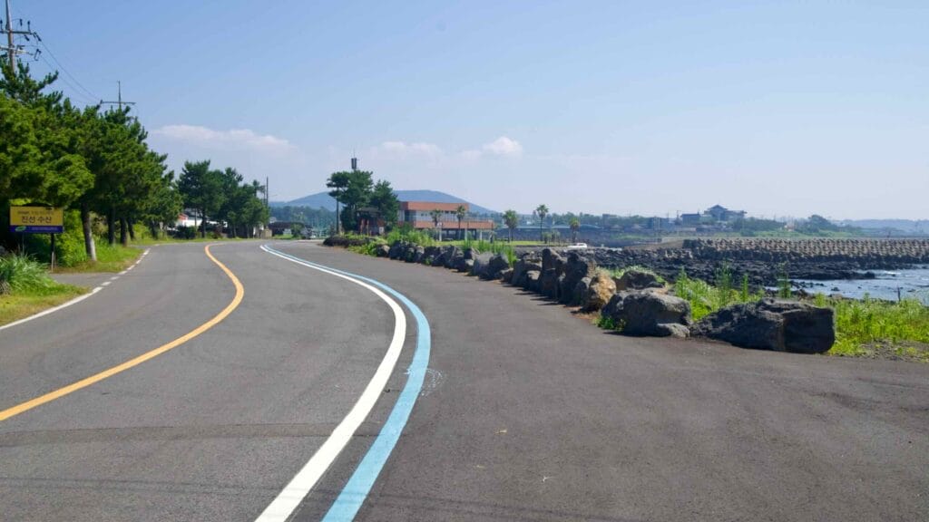 A coastal road with a blue bike lane curves toward breakwaters near Taeheung.
