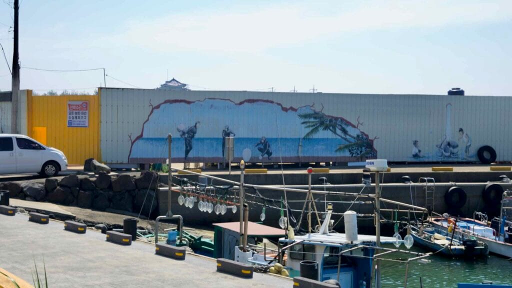Container murals and squid‑fishing lights line the quay at Taeheung harbor.