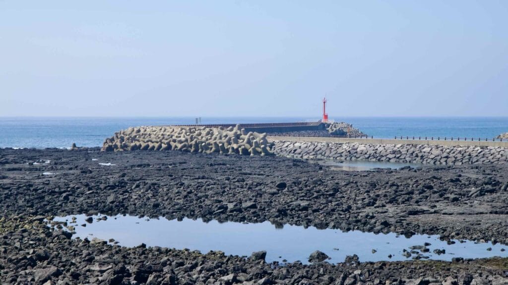 Tide pools reflect the sky below tetrapod breakwaters and a red lighthouse at Taeheung.