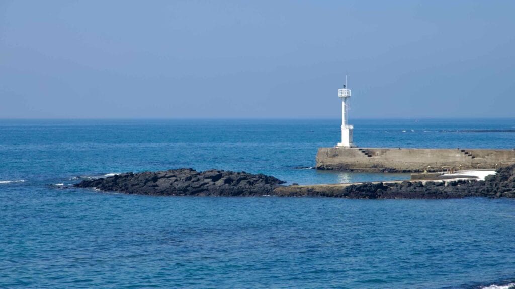 A white harbor beacon stands on the breakwater near Shiheung-ri under clear skies.