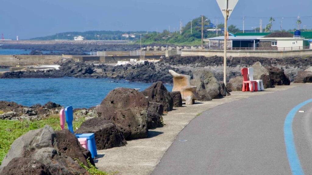 Chairs line a lava-rock walkway by the water at Taeheung with harbor walls in the distance.