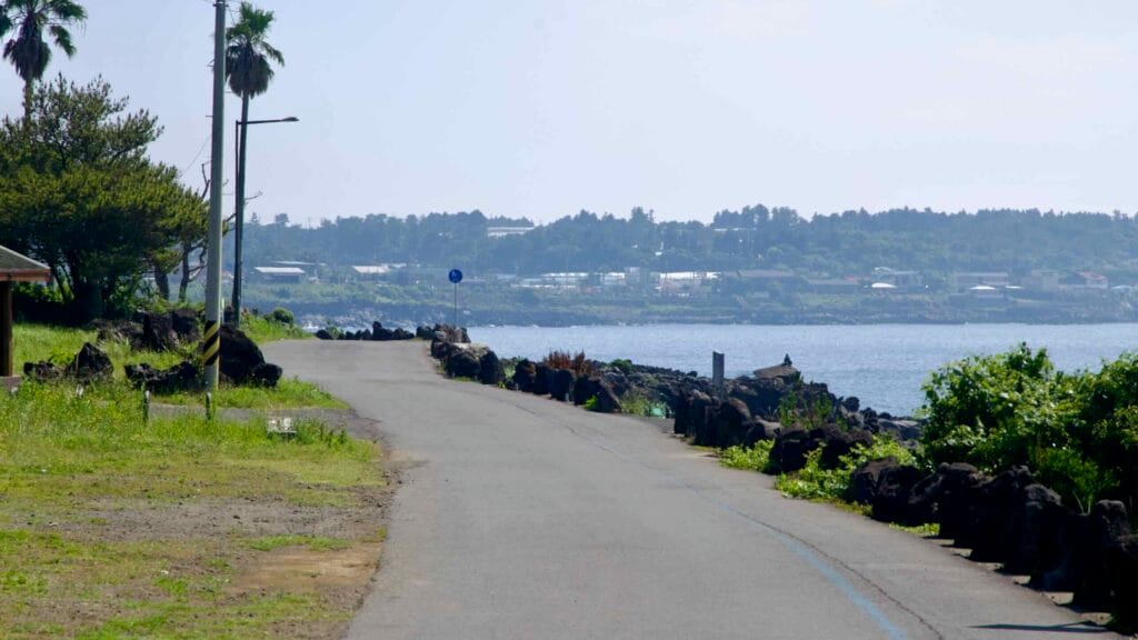 A coastal road curves along the Sinheung-ri shoreline in Namwon, with basalt rocks and low waves lining the coast.