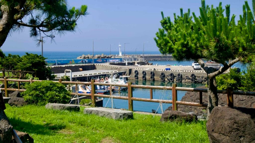 Fishing boats rest in the basin at Sinheung-ri Port below a breakwater and lighthouse.