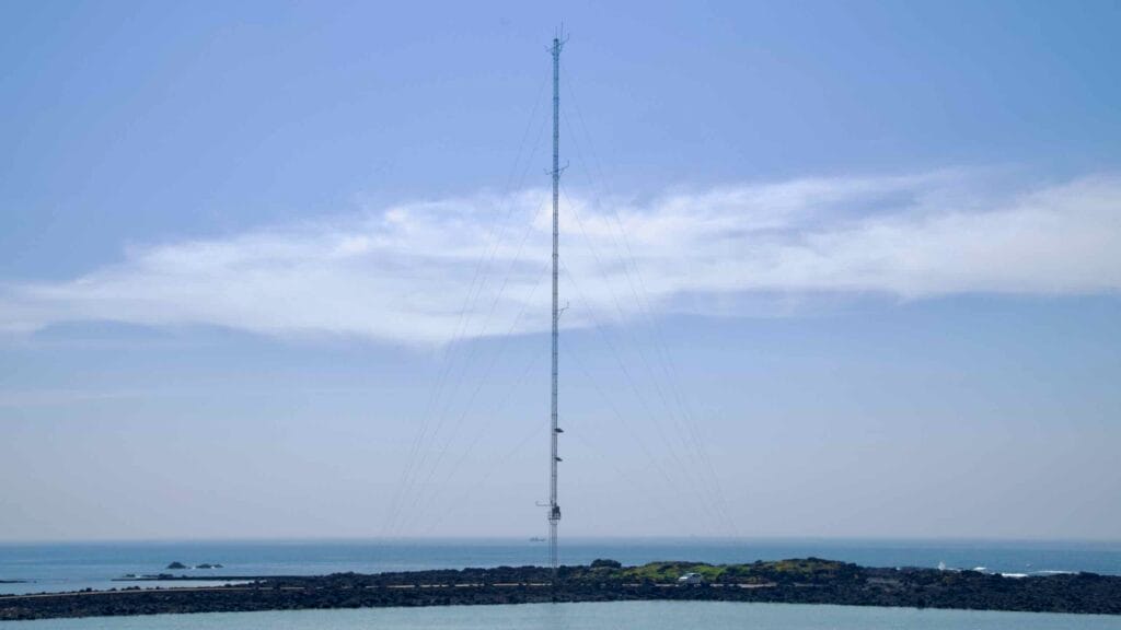 Green slopes descend to basalt reefs near Sinheung-ri where low tide reveals rock pools and gentle waves.