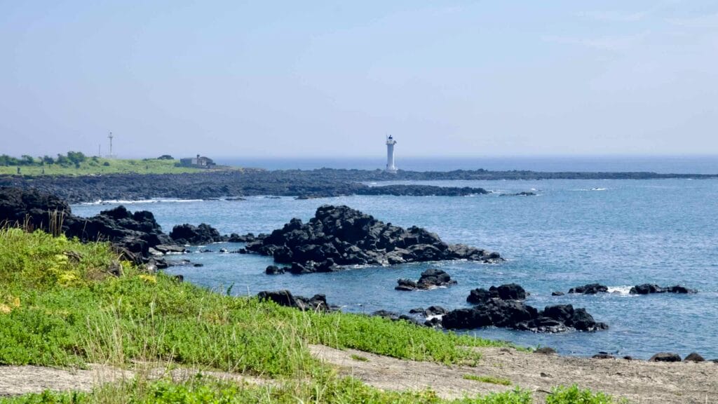 A white lighthouse beyond the basalt rocks of White Hill on Pyoseon’s coast.