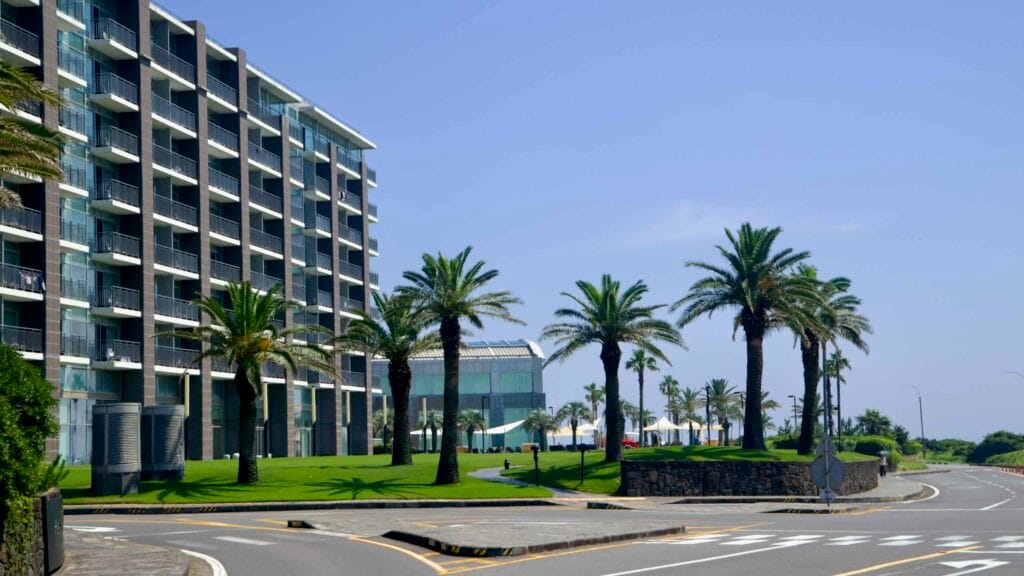 A glass‑fronted resort and palm‑lined lawns near Pyoseon Beach.