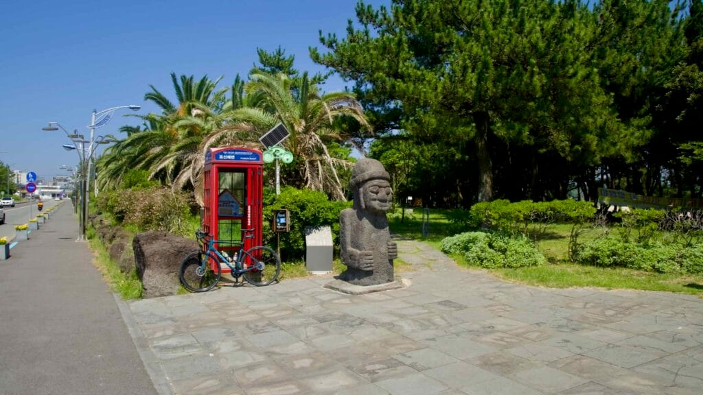 The Pyoseon Beach promenade runs past a red phone booth and dolhareubang statue.