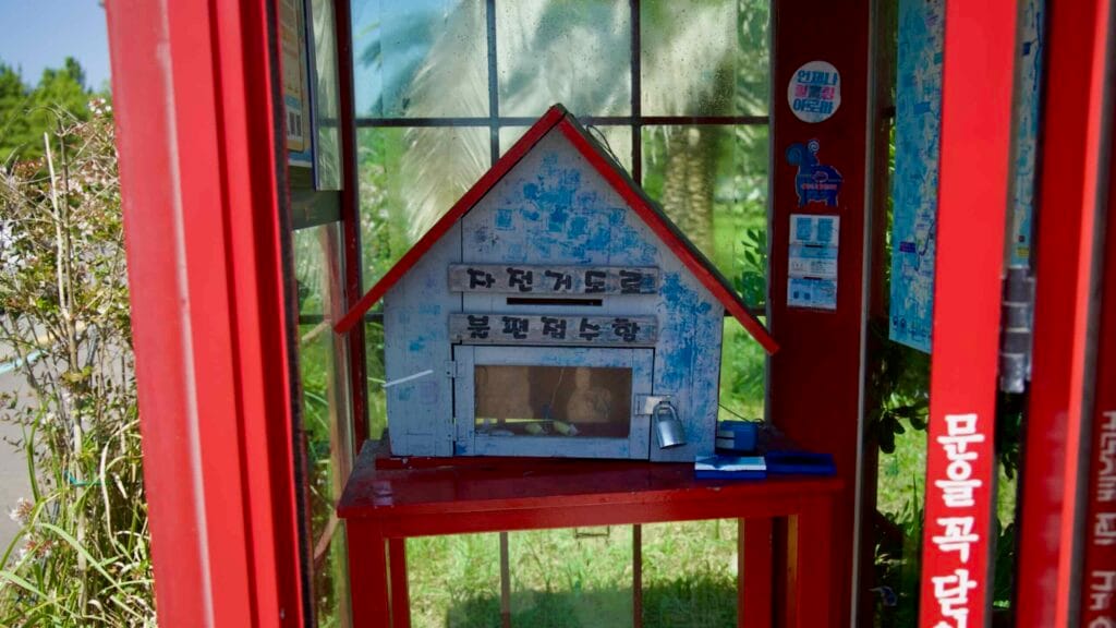 Inside the red phone booth at Pyoseon Beach, a house-shaped locker serves cyclists with maps.