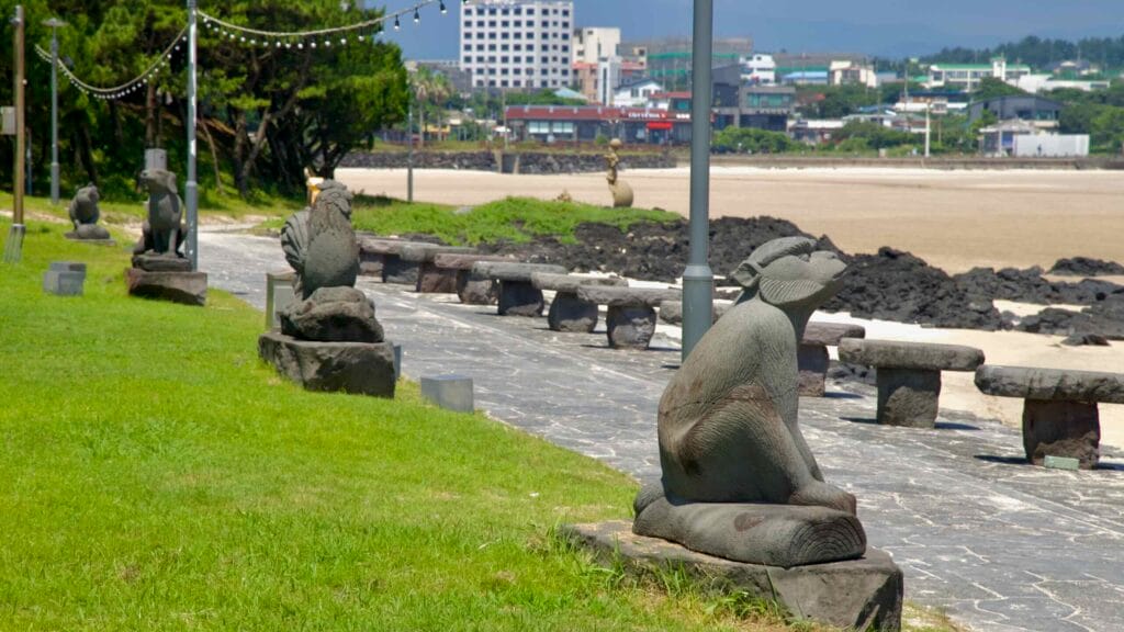 Basalt animal sculptures line the promenade at Pyoseon Beach with broad tidal flats stretching beyond.