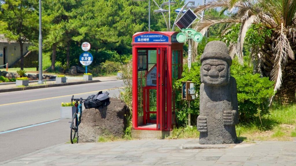 A dolhareubang statue and red phone booth stand at the entrance to Pyoseon Beach.