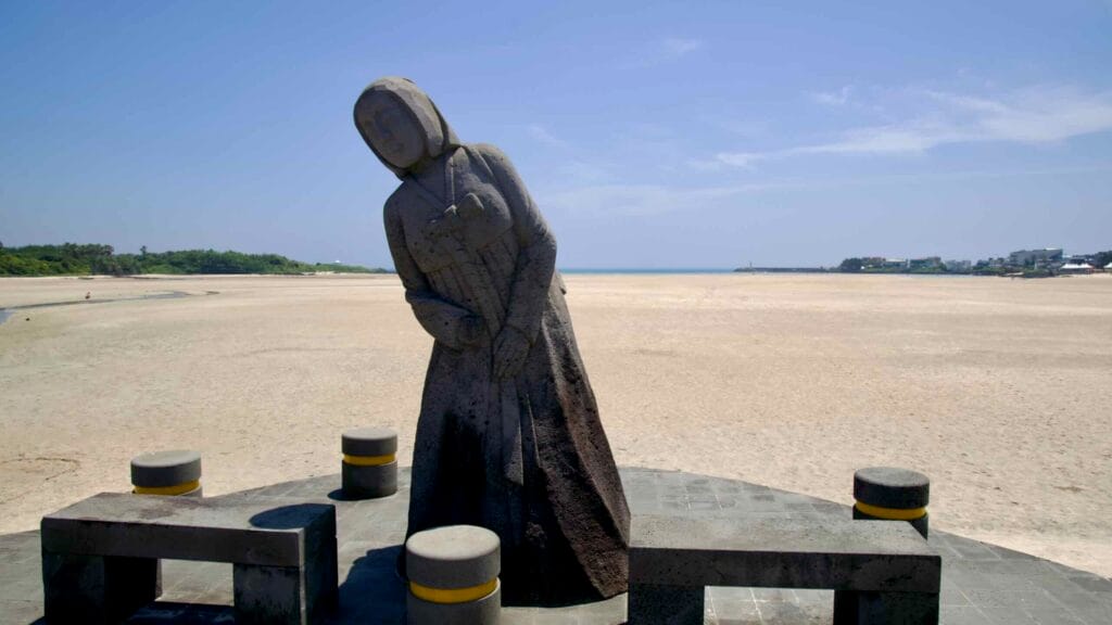 A stone figure stands by benches facing the broad tidal flats at Pyoseon.