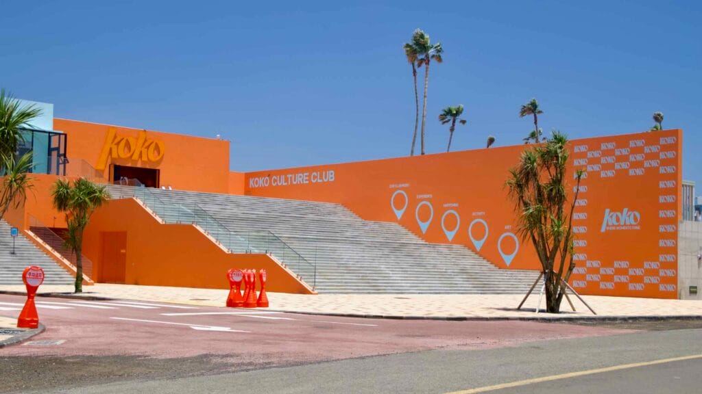 The KoKo Culture Club’s orange steps and branded walls face the road beneath tall palms.