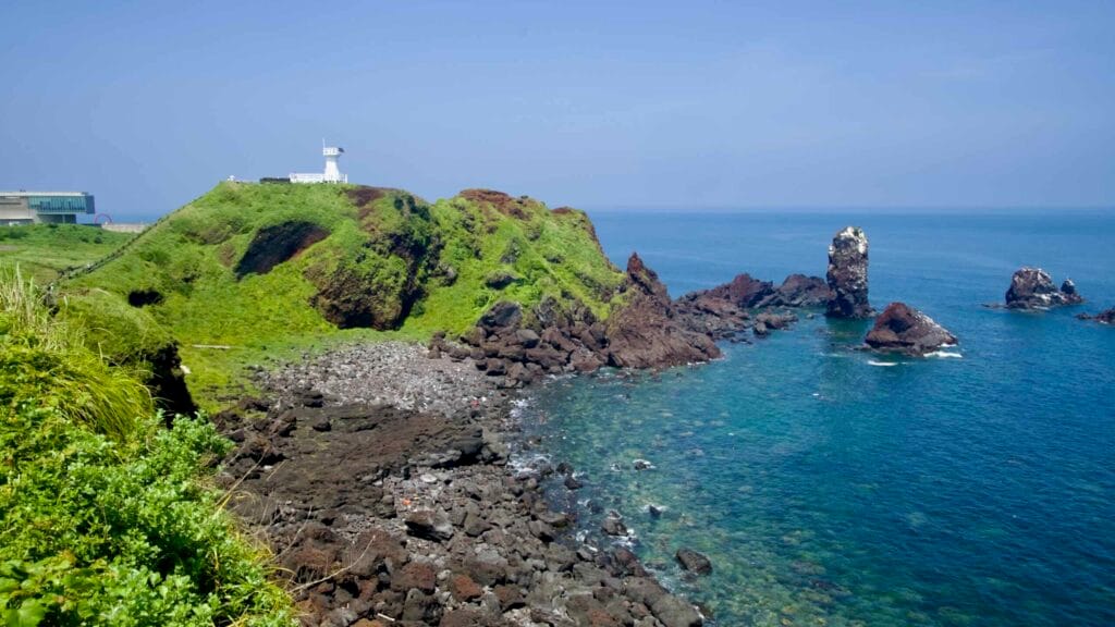 Seopjikoji’s lighthouse tops Bulgeun Oreum above a clear cove and Standing Rock.