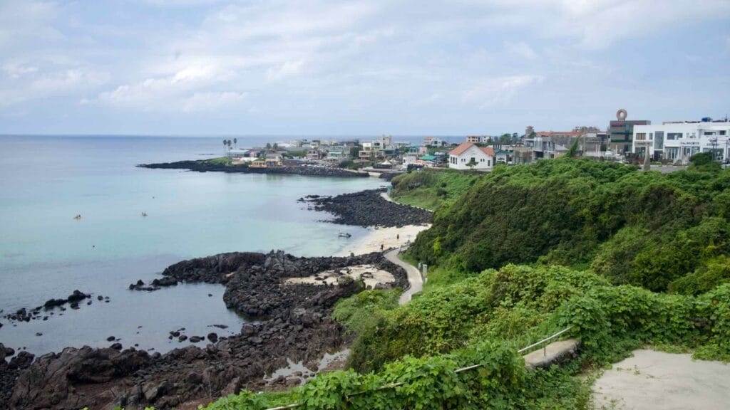 Curving Handam shoreline with clear water, basalt reefs, and kayakers offshore.