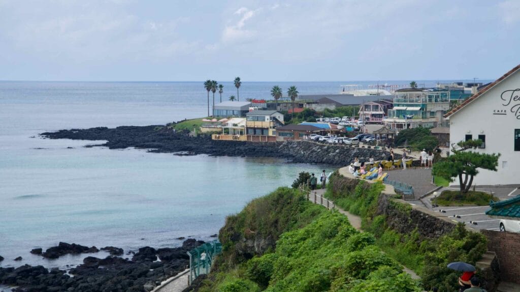 Cafés and palms overlook Handam’s clear bay while the path traces the basalt shoreline.
