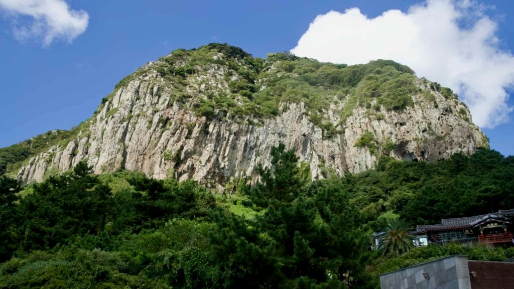 Sheer volcanic wall of Sanbangsan above forest canopy.