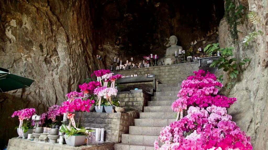 Inside Bomunsa cave, a Buddha sits amid bright pink orchids and candle offerings in Jeju.