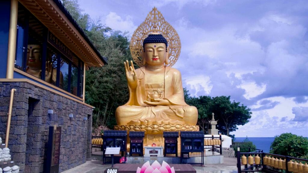 A large golden Buddha statue at Bomunsa on Sanbangsan, with a halo and prayer offerings at its base.