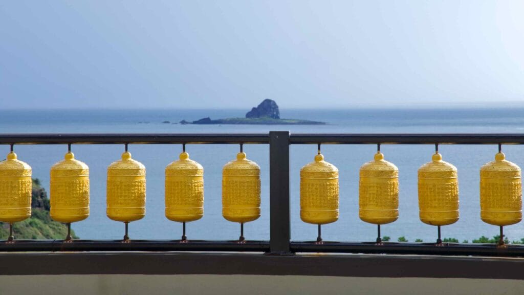 Golden prayer wheels line a terrace railing at Bomunsa, with a sea view of Hyeongje Islet.