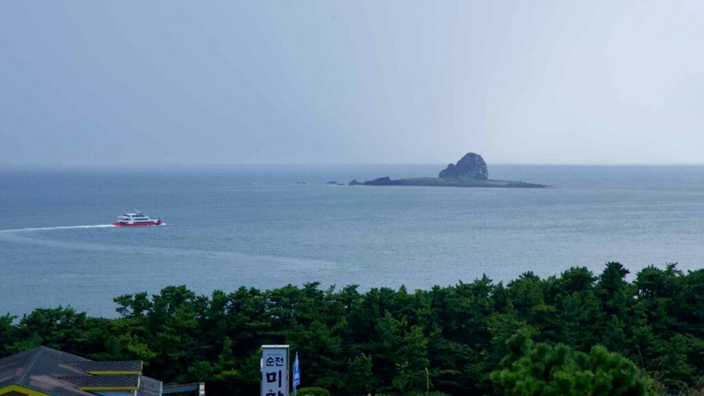 A red and white ferry passes an Hyeongje Islet, viewed from Bomunsa Temple.