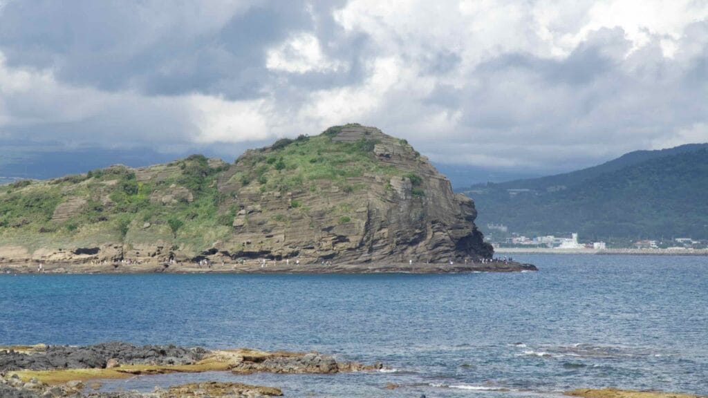 The rocky green slopes of Yongmeori Coast jut into the sea near Sanbangsan, with visitors on tidal rocks.
