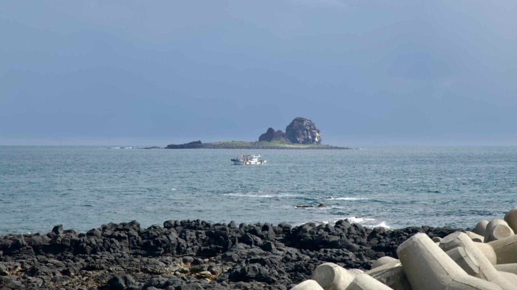 A fishing boat sails past a Hyeongje Islet off Sanbangsan’s volcanic coast.