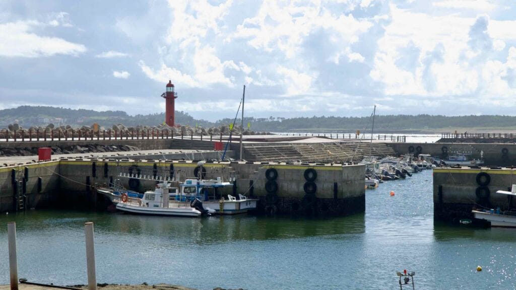 Sagye Port on Jeju's southern coast with moored boats and a red lighthouse.