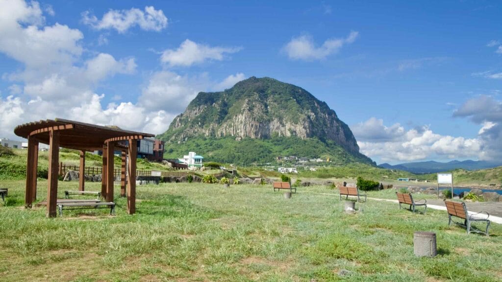 Fishing boats dock inside a concrete harbor on Jeju’s south shore, with a red lighthouse standing guard.