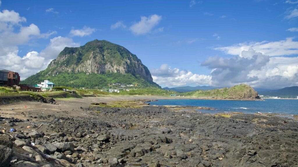 Sanbangsan’s sheer dome rises beside Yongmeori, above basalt tidelands of pools and ledges toward sea.