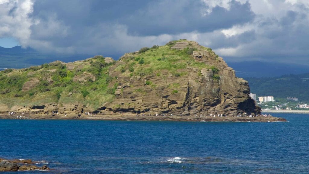 Close tuff and ash layers form ledges along Yongmeori, its green crown standing over blue water.