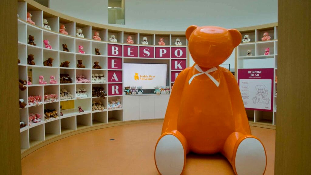Giant orange teddy bear statue with plush‑filled shelves at Bespoke Bear.