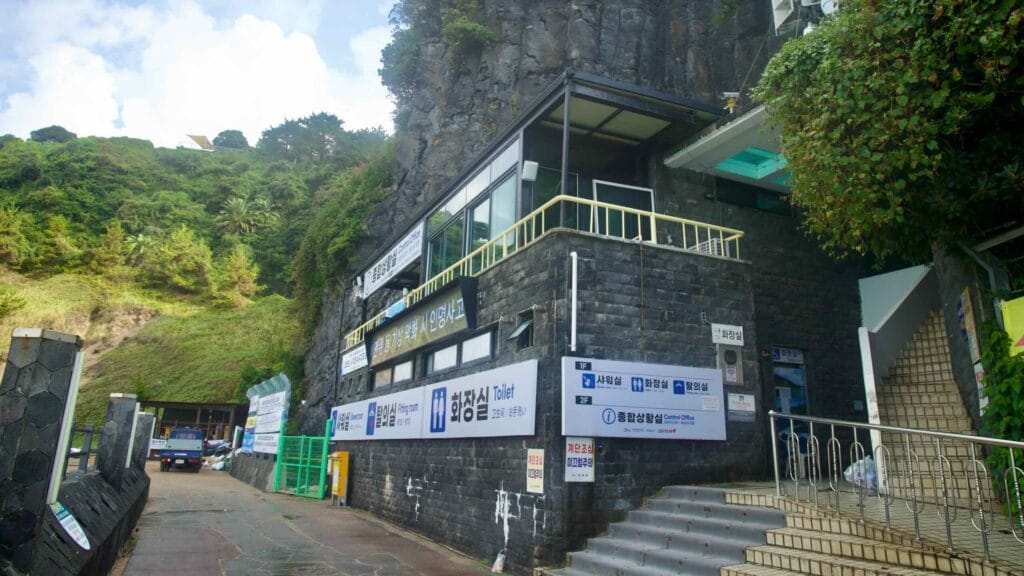 A cliff-base building at Jungmun houses showers and an office, with stairs down to the sand.