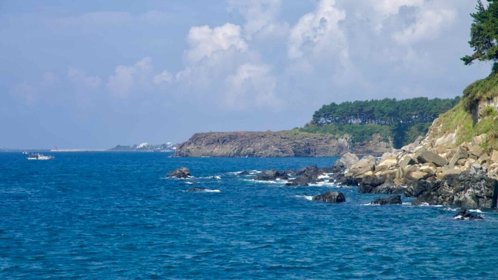 A rocky shoreline and blue water stretch south of Seogwipo Port.