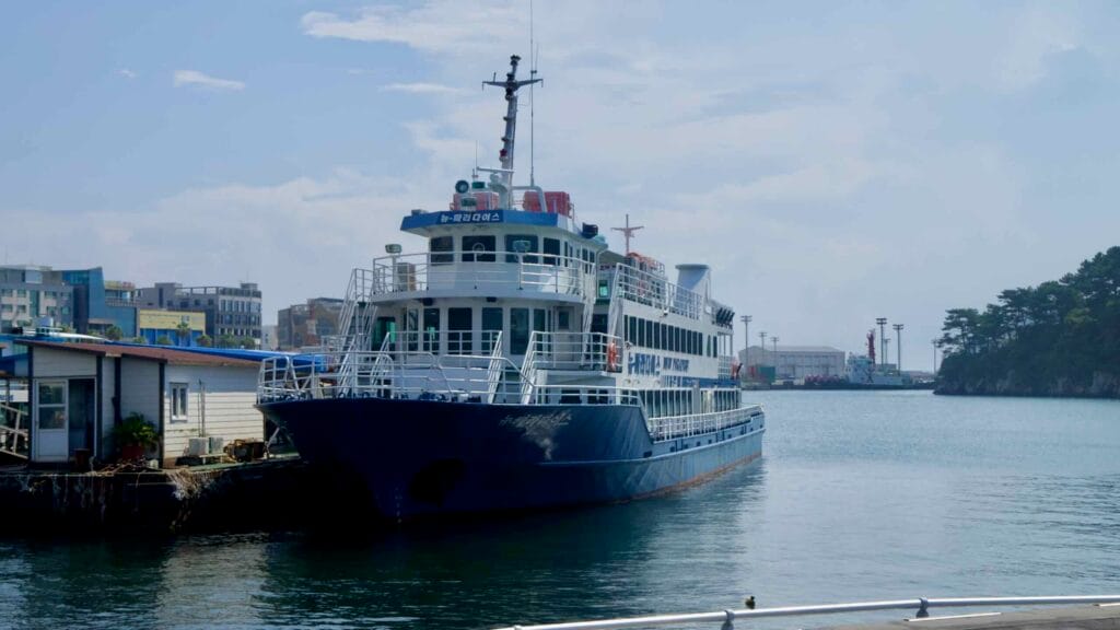 A white‑and‑blue sightseeing vessel is moored inside Seogwipo Port.