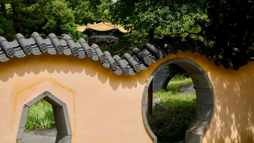 Curved tiled roofs top a yellow garden wall with moon gates near Jeongbang Falls.