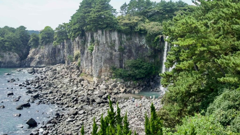 Basalt cliffs and a boulder shore surround the basin beneath Jeongbang Falls.