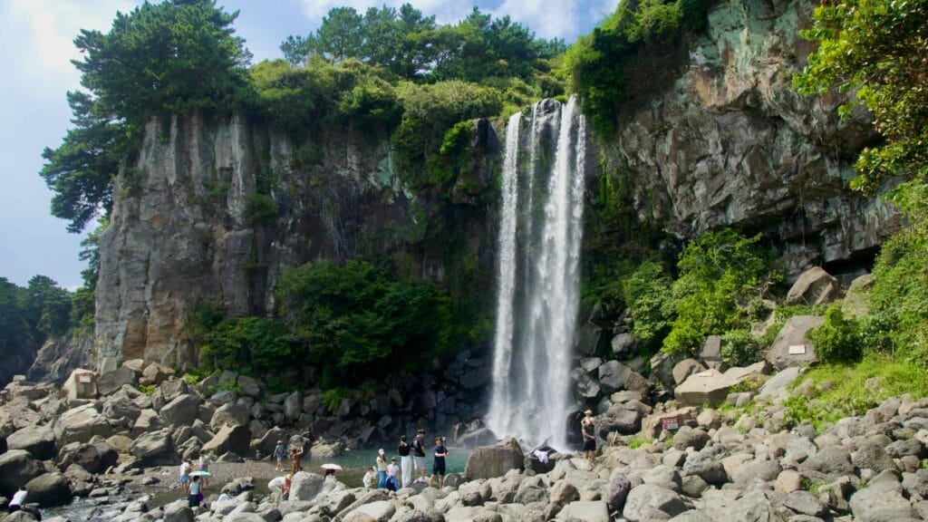 Visitors gather on boulders at the base of Jeongbang Falls.