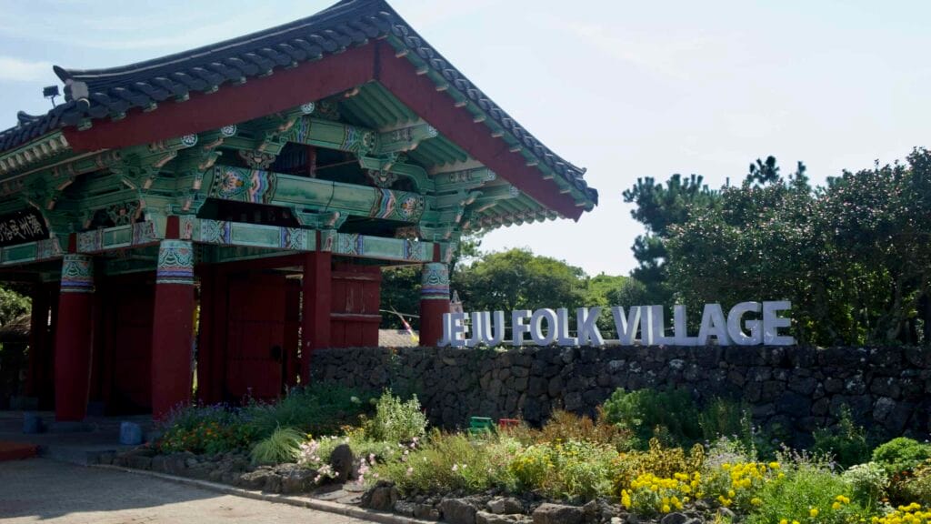 The main gate of Jeju Folk Village rises above stone walls and flowers.