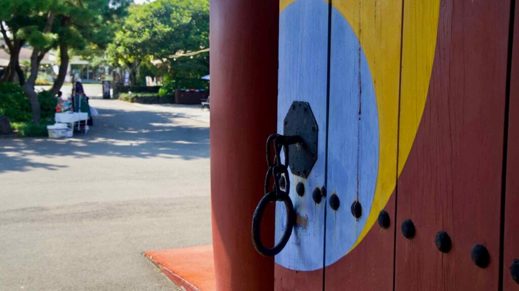 A painted taeguk and iron ring detail the gate at Jeju Folk Village.