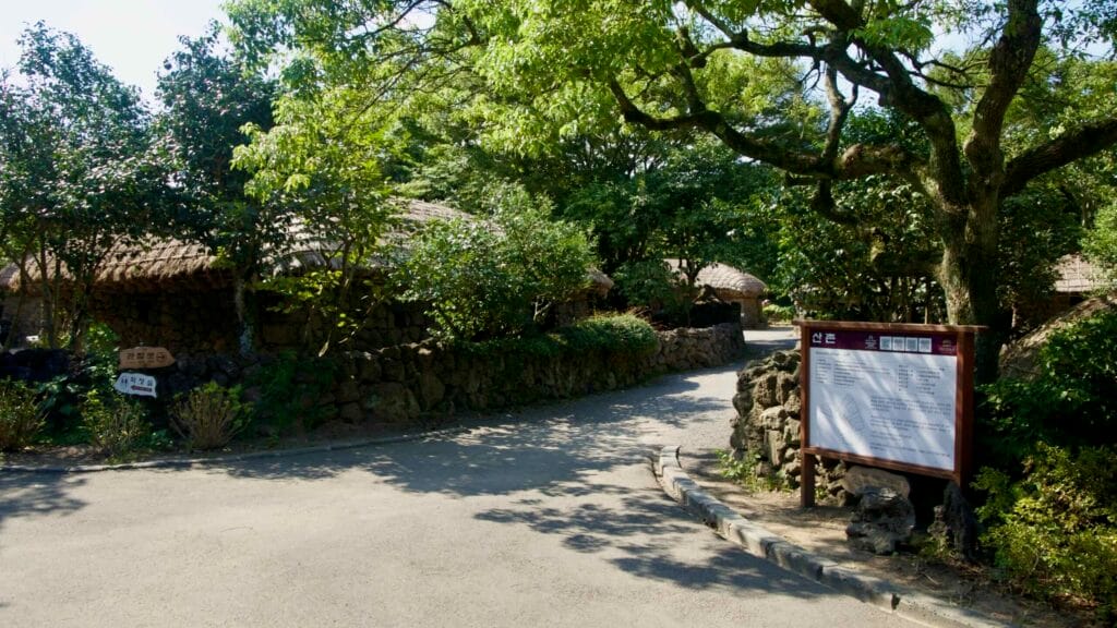 A signboard and curving path lead between stone walls and thatched cottages in Jeju Folk Village’s mountain zone.